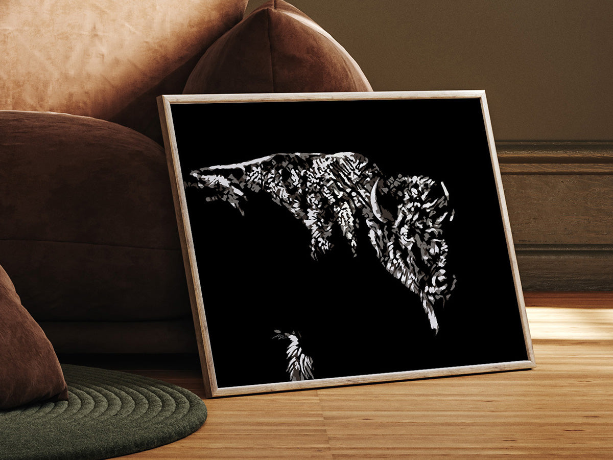 A framed black and white artwork of a bison, titled 'Modern Bison', placed on a floor next to a couch.