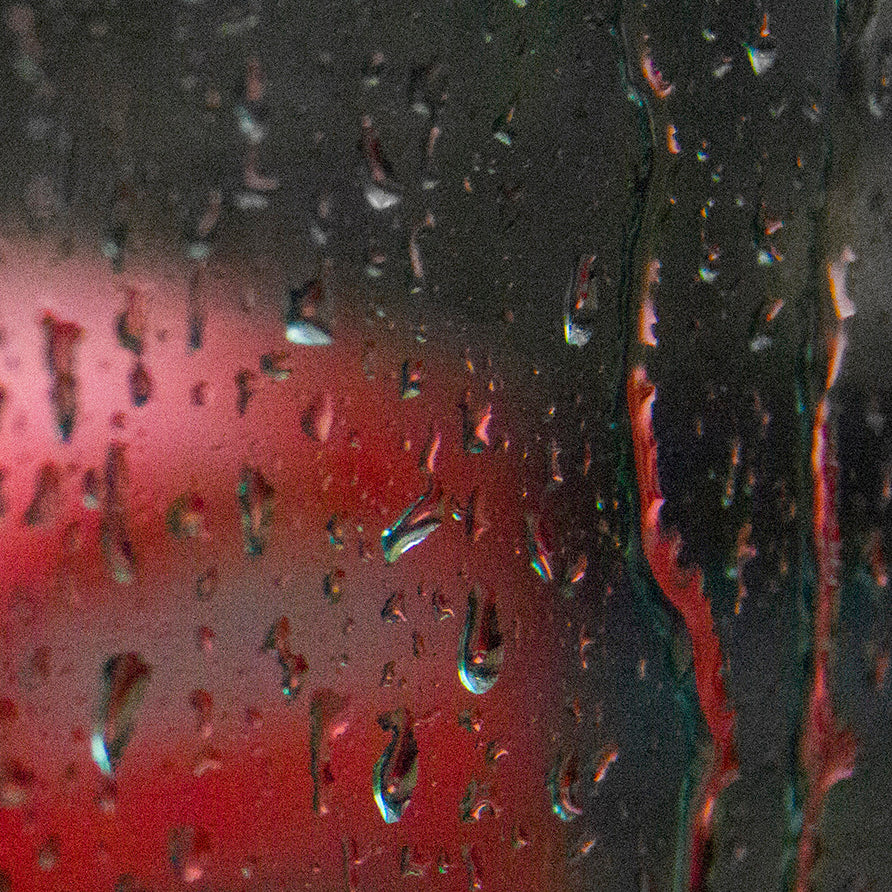 Rainy window with a blurred red postbox visible in the background, creating a moody and nostalgic atmosphere.